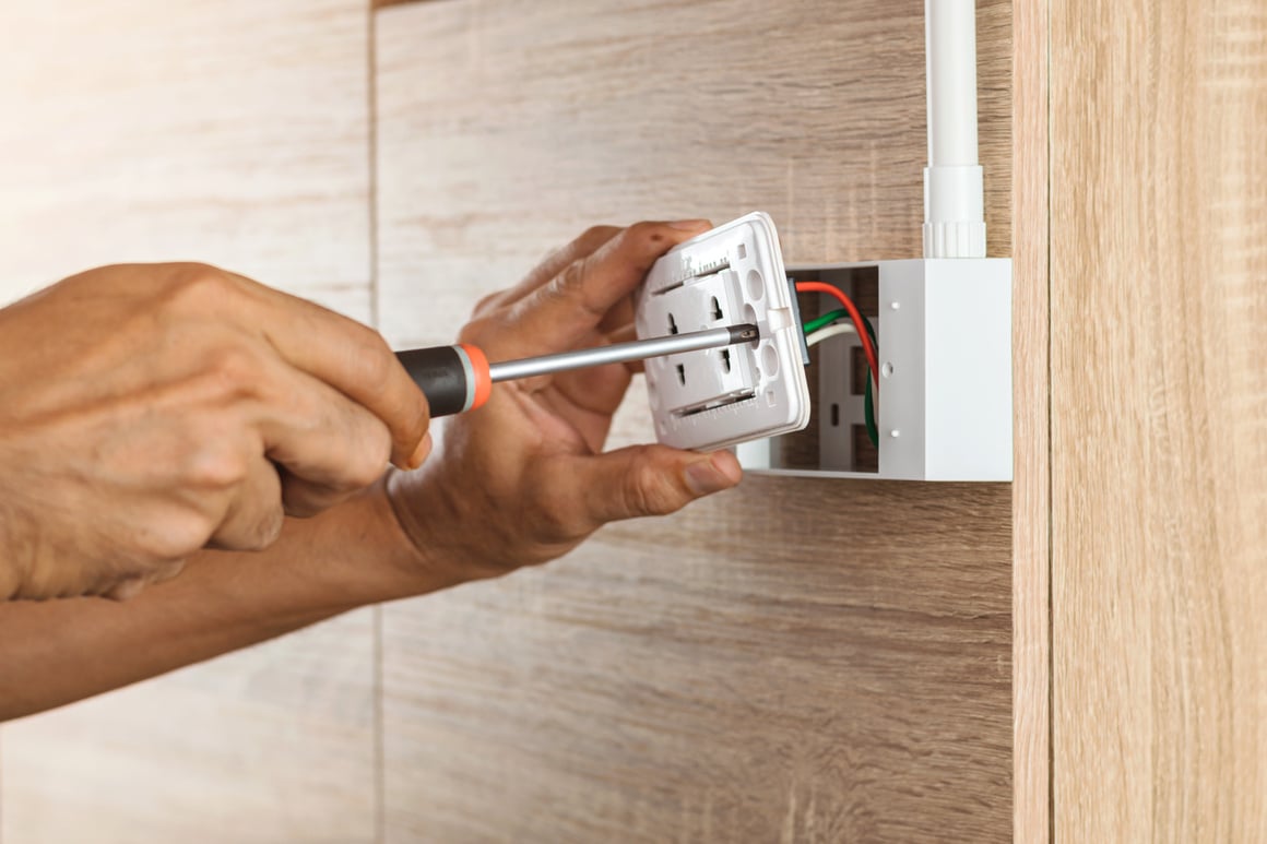 Electrician is using a screwdriver to install a power outlet